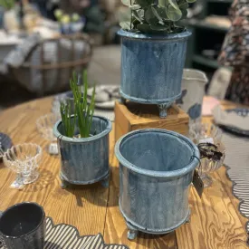 Blå glaserad kruka på fyra tassar med grön växt i mässmonter