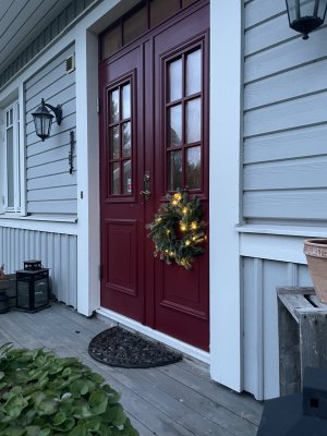Warmly lit winter wreath on a classic deep red double front door of a country style house during evening twilight