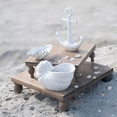 Fat ostron tillsammans med andra maritima detaljer på små naturfärgade piedestaler på en strand.
