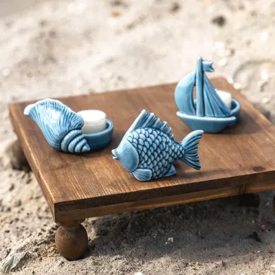 Snäckformad blå vrämeljushållare tillsammans med andra maritima detaljer i blå keramik på en strand.
