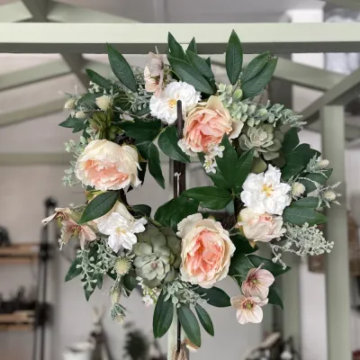 Fyllig aprikos krans med pioner och suckulenter upphängd i växthusmiljö