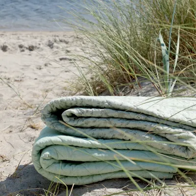 Grön quiltad pläd Aix från Chic Antique i full sol på en strand.