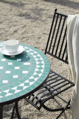 Svart metallstol vid mosaikbord utomhus i lantlig miljö