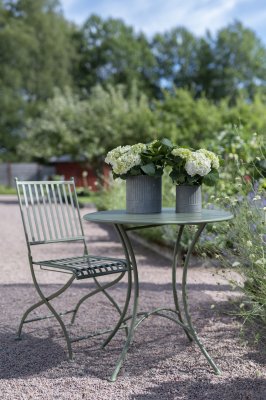 Olivgrönt cafébord i metall 70 cm diameter i lantlig trädgård