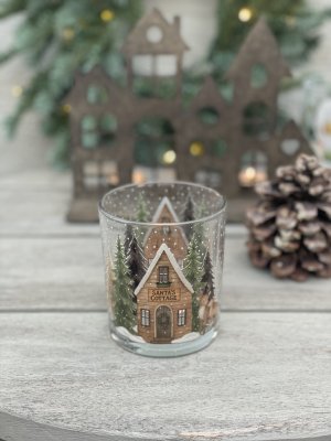 Närbild i klart fokus på julljuset Rustic Cottage från Majas Cottage, stylad i en vintrig miljö framför ett tänt dekorationshus