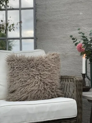 Fluffigt och lurvigt lockigt kuddfodral Curly i sandfärg från Fondaco, stylat i en vit korgstol med ett tänt ljus och en dahlia 