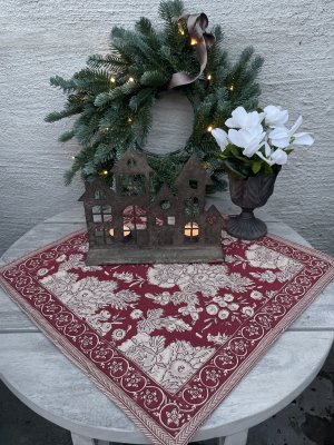 Tygservett Sonia Röd 45x45 cm från Fondaco med botaniskt mönster under ett dekorativt ljushus i metall på ett dukat höstbord