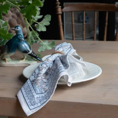 The Dante cloth napkin in a blue pattern from Fondaco in a napkin ring on a table.
