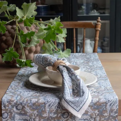 The Dante cloth napkin in a blue pattern together with the runner from Fondaco in the same pattern set on a table.