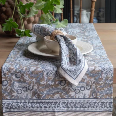 The Dante runner with a blue pattern on a table together with the cloth napkin in the same series, from Fondaco.