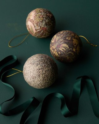 Julgranskulor Delight med gammaldags vintagemotiv ligger på en mörkgrön duk med ett dekorativt grönt band slingrande framför frå