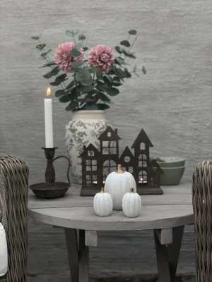 Höstdukning på ett runt grått träbord i lantlig stil med tre vita pumpor med guldkvistar, en mönstrad urna med rosa dahlior, en 