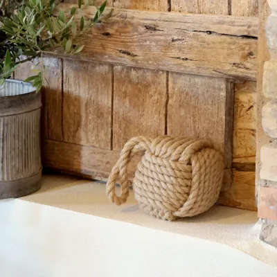 Maritime rope door holder placed at a rustic interior door on a stone floor.