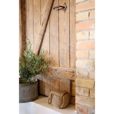 Interior detail with a nautical feel; doorstop in braided hemp standing by a rustic door.
