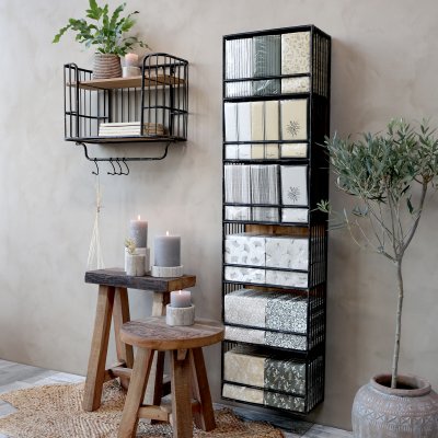 Hög smal vägghylla i antiksvart metall med träbakstycke från Chic Antique fylld med servetter bredvid rustika träpallar och tänd
