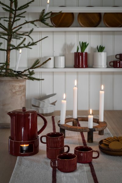 Röda glöggmuggar och värmare med kanna för julens glöggmingel uppdukat i en lantlig miljö, från Ernst.