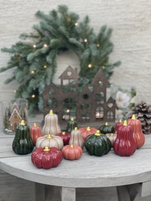 En stor samling av dekorativa keramikpumpar i hallon, rost, beige och mörkgrönt med glänsande guldstjälkar, stylade på ett grått